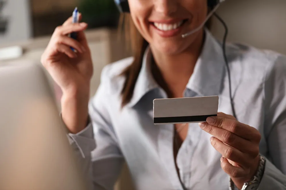 A smiling woman wearing a headset holds up a blank plastic card and a pen