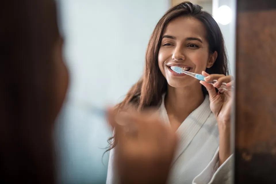 A smiling woman brushing her teeth in front of a mirror