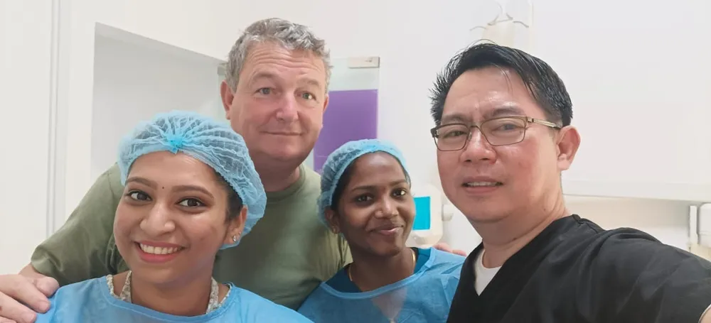 Four people smiling together in a dental room, two wearing blue caps and gowns
