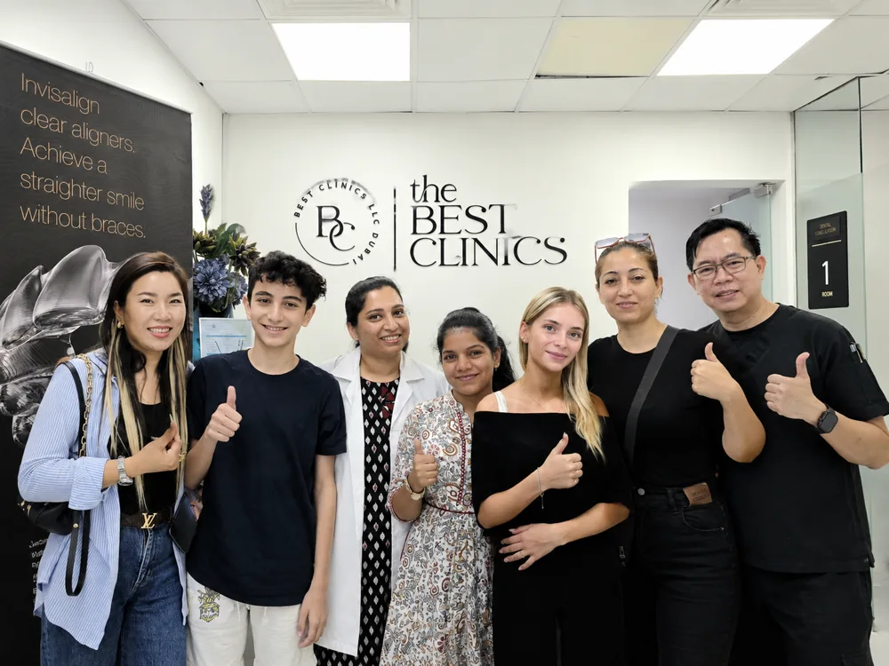 Seven smiling people, some giving a thumbs up, standing in front of a wall sign reading “the Best Clinics”