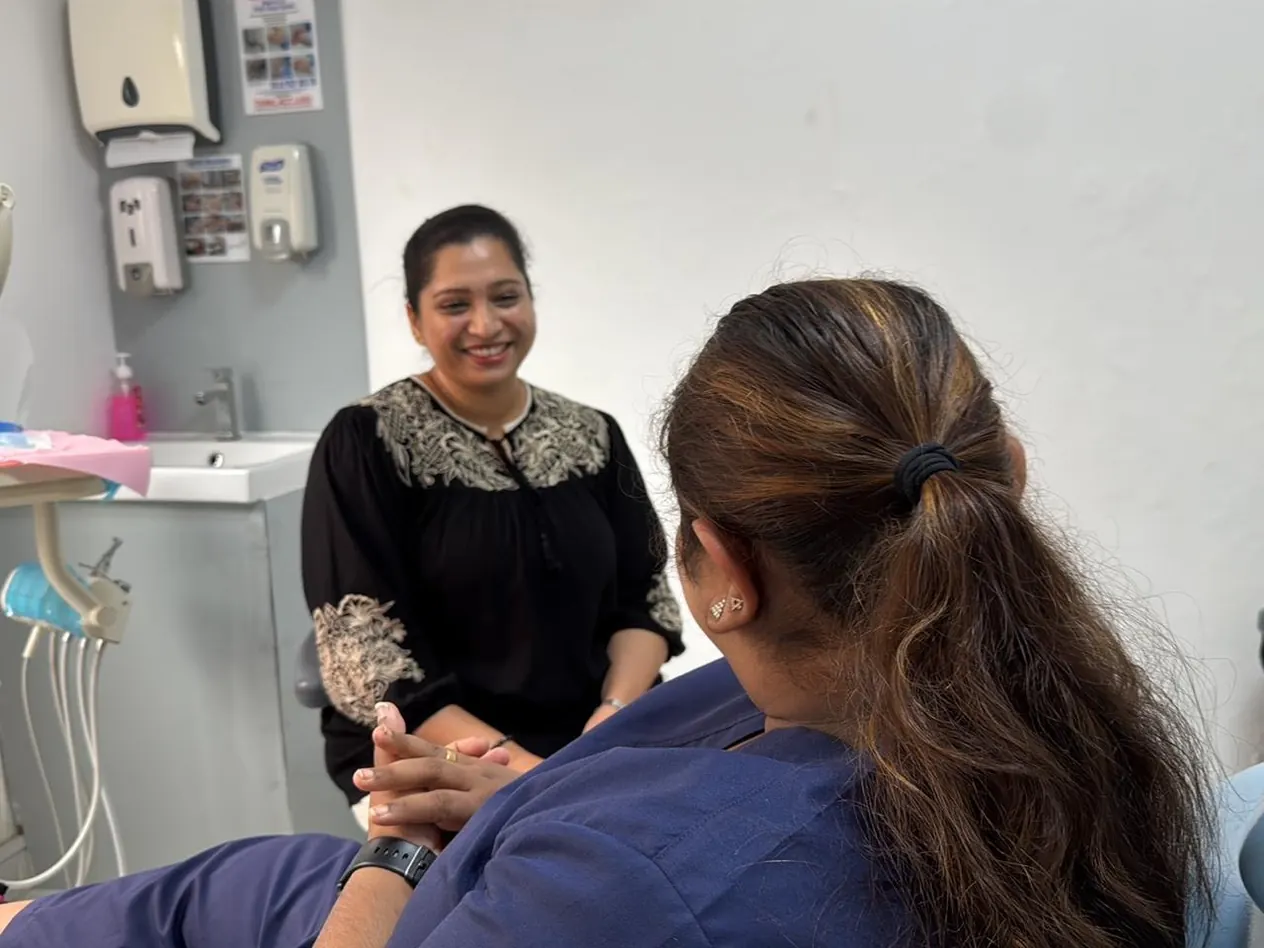 Woman in navy scrubs seated in a dental chair, facing a smiling woman, at Best Dental Clinic