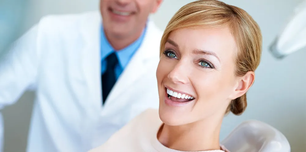 A smiling woman in a dental chair with a dentist standing behind her